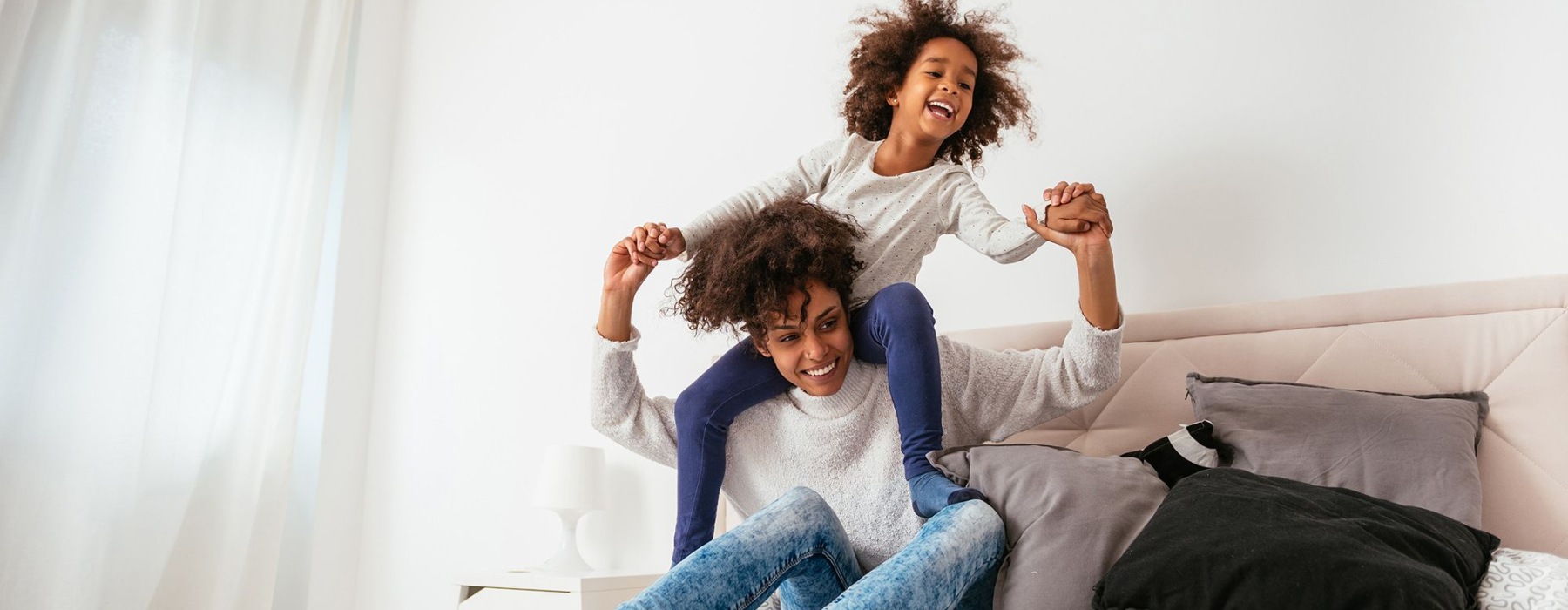 mother and daughter happily play on a large bed