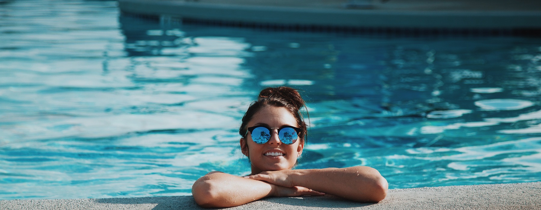 lifestyle image of a woman leaning on the edge of a pool with sunglasses on her head