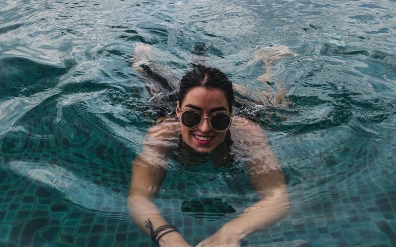 lifestyle image of a young women in a pool with sunglasses on as she lays in the shallow water